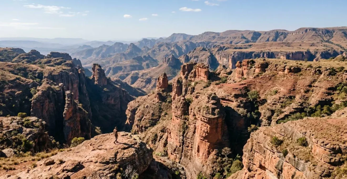 Vue aérienne d'un canyon malgache aux parois ocre-rougeâtres avec une petite silhouette humaine sur une crête rocheuse