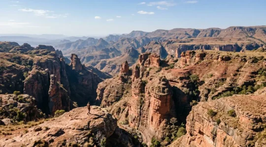 Vue aérienne d'un canyon malgache aux parois ocre-rougeâtres avec une petite silhouette humaine sur une crête rocheuse