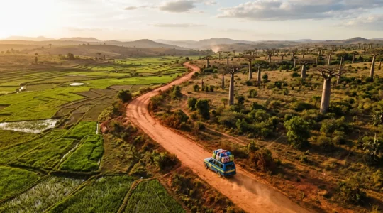 Vue aérienne d'un taxi-brousse coloré traversant une route poussiéreuse malgache entre rizières et baobabs