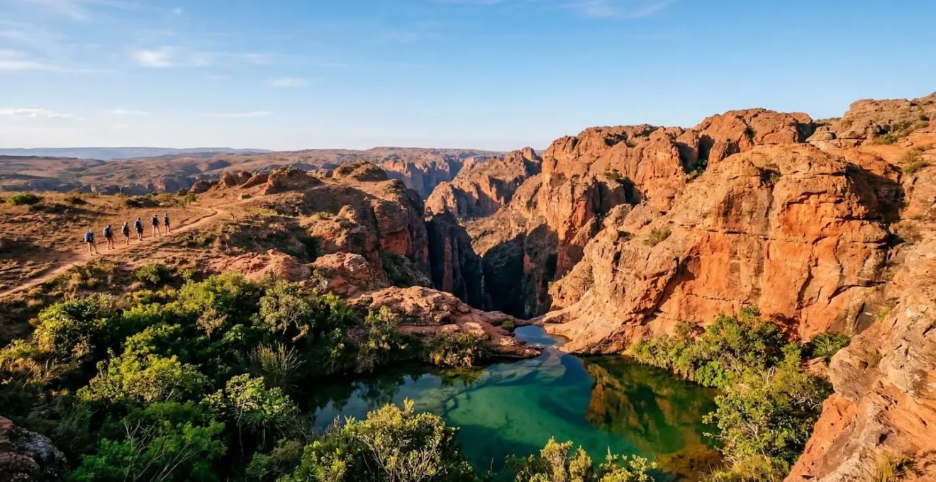 Vue panoramique des canyons de grès rouge de l'Isalo avec une piscine naturelle turquoise au premier plan et des randonneurs contemplant le paysage