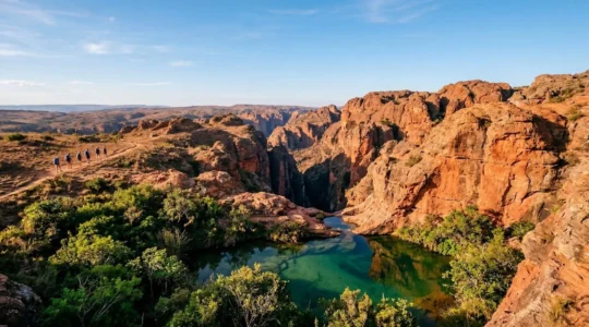 Vue panoramique des canyons de grès rouge de l'Isalo avec une piscine naturelle turquoise au premier plan et des randonneurs contemplant le paysage