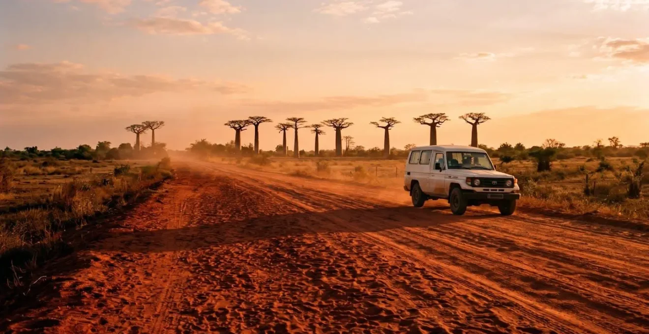 Piste de latérite rouge avec véhicule 4x4 et baobabs géants à l'horizon au coucher du soleil